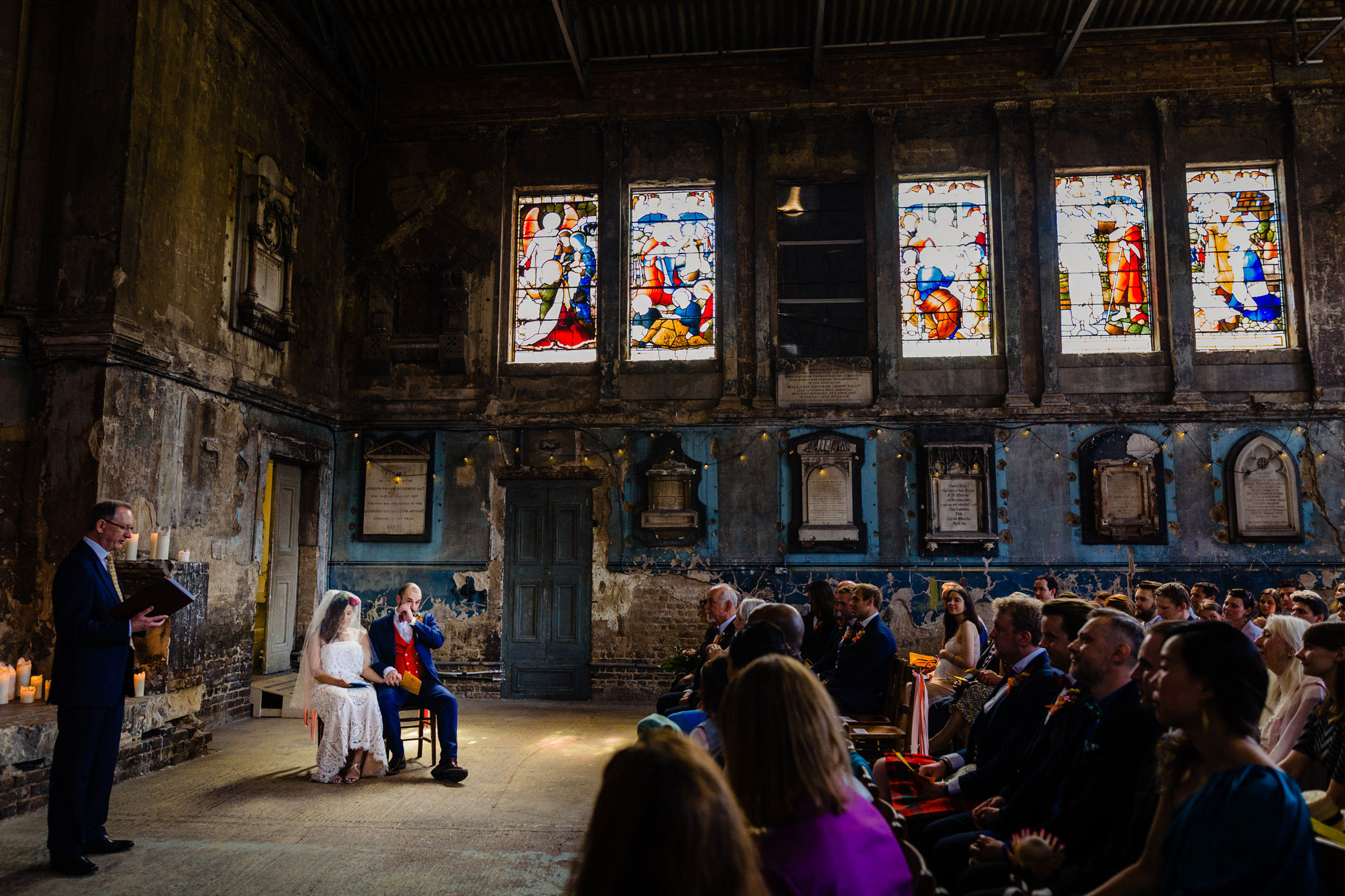 a wide shot of a wedding in a beautiful and slightly dilapidated old chapel. the groom is wiping a tear from his eye.