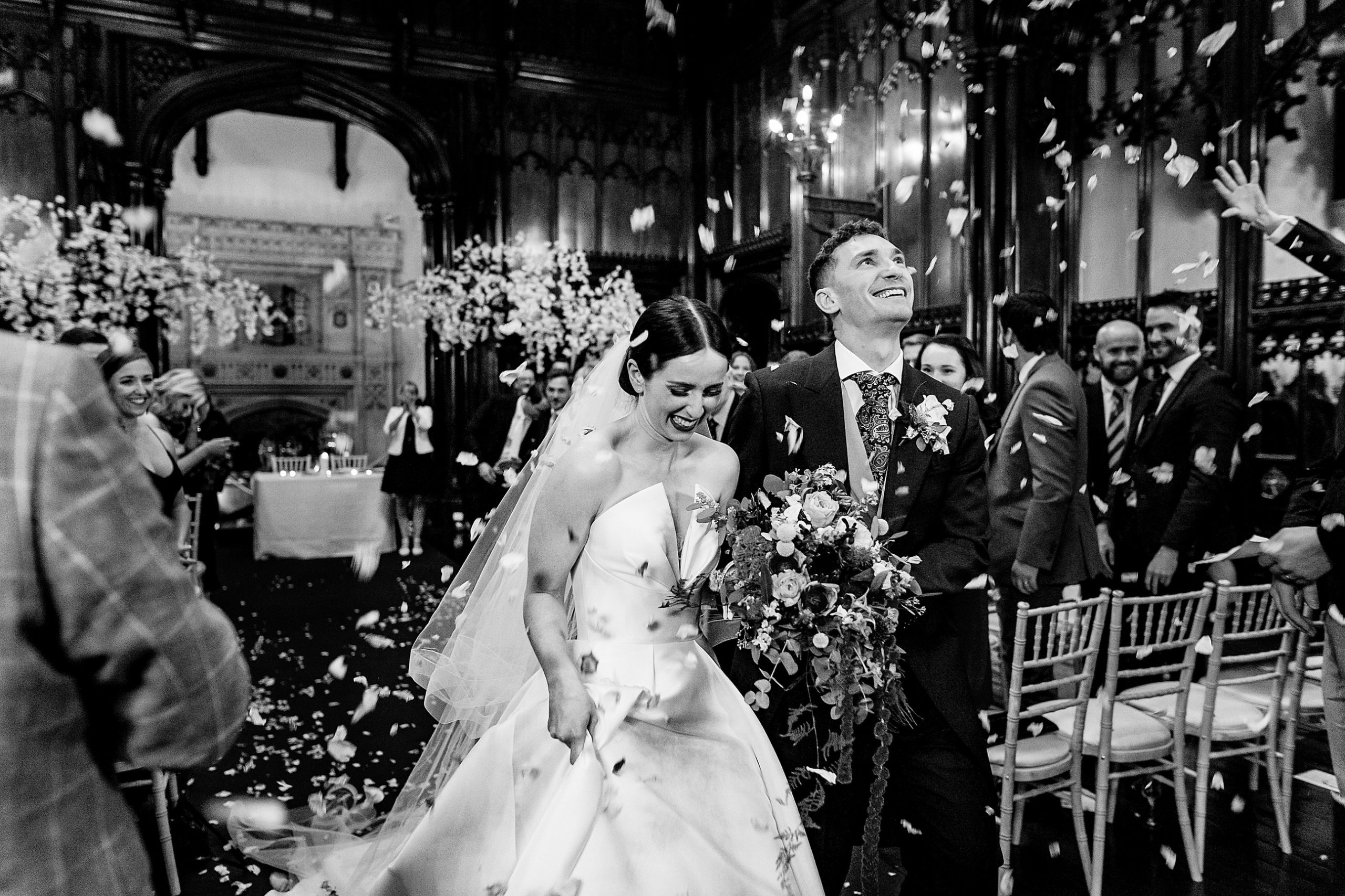black and white photo of a bride and groom leaving their wedding ceremony whilst being showered in confetti. allerton castle wedding photography by emma and rich.