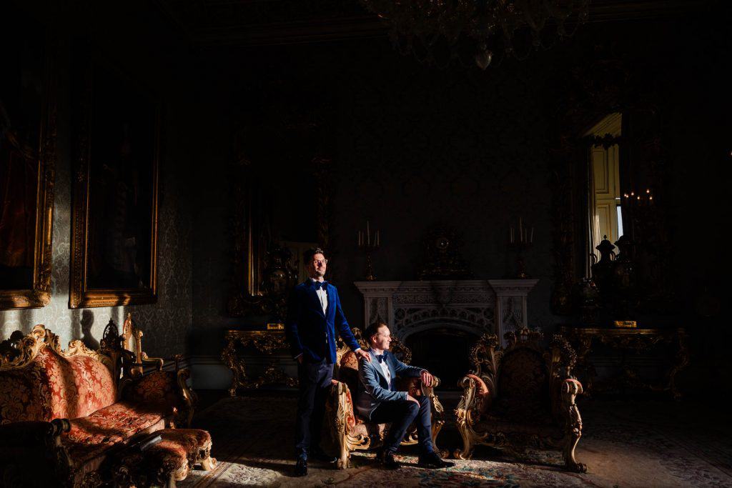 two recently married men pose together in a sunbeam in an ornate Georgian drawing room. Allerton Castle wedding photography by emma and rich.